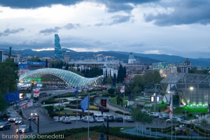sunset view of the Bridge of Peace with aerial tramway terminal near Rike Park and Europe Square in Tbilisi, Georgia,with skyscraper on middleground and hills on background